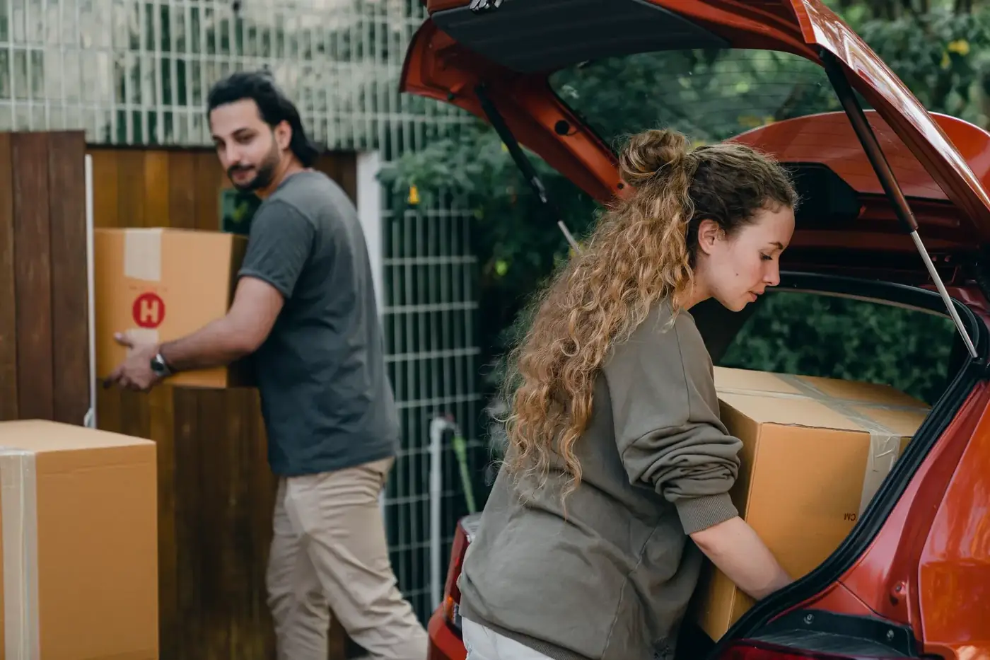 A couple unloading moving boxes from a car outside a home