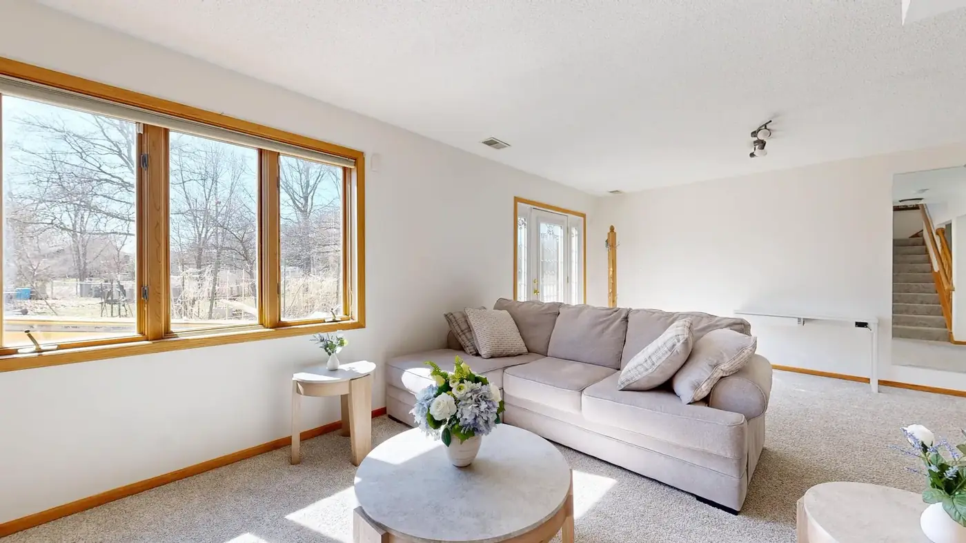 A bright, staged living room with a beige sofa and large windows